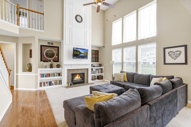 living room with baseboards, a ceiling fan, a high ceiling, stairway, and a tile fireplace