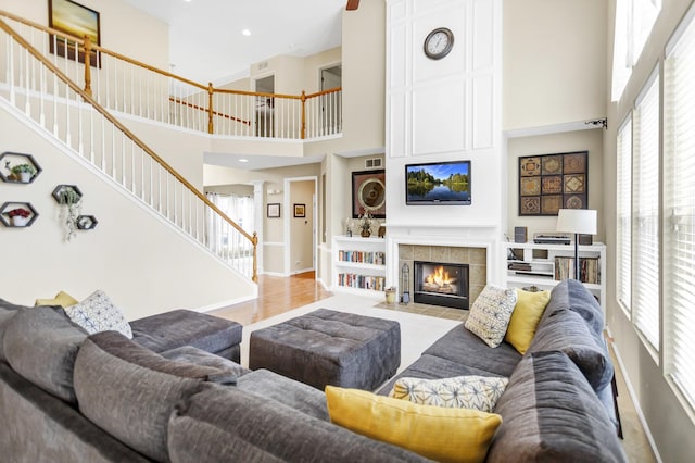 living area featuring baseboards, a tile fireplace, a high ceiling, and stairway