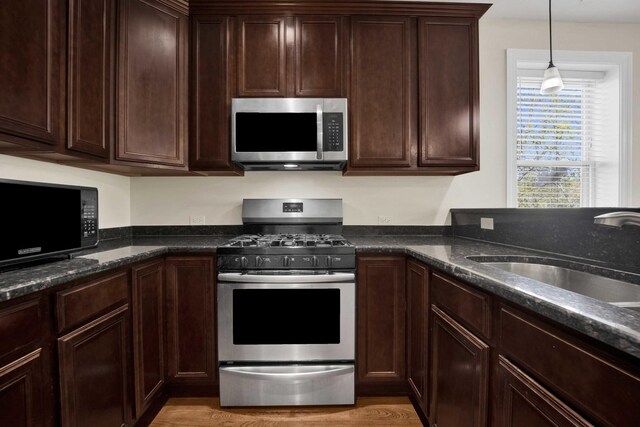 4538 S Calumet Ave Unit 3N, Chicago, IL 60653 - kitchen with dark stone counters, stainless steel appliances, dark brown cabinets, a sink, and pendant lighting