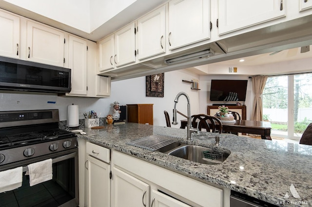 kitchen featuring stainless steel appliances, a sink, light stone counters, white cabinets, and recessed lighting