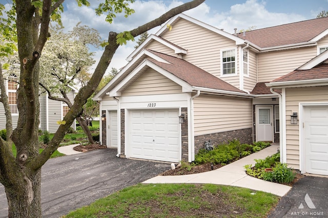 multi unit property with roof with shingles, driveway, a garage, and stone siding