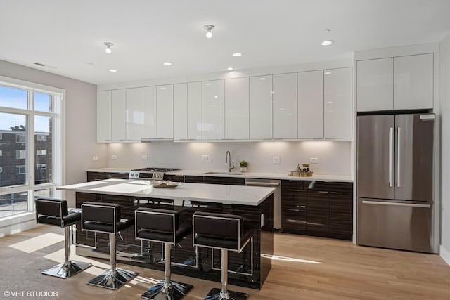 kitchen featuring stainless steel appliances, a sink, modern cabinets, a kitchen bar, and white cabinetry