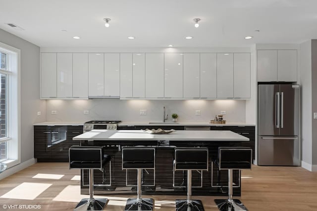 kitchen with a sink, light wood-type flooring, modern cabinets, stainless steel appliances, and baseboards