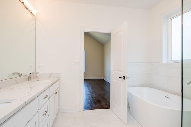 full bathroom featuring a sink, double vanity, vaulted ceiling, baseboards, and a freestanding tub