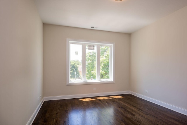 spare room featuring visible vents, baseboards, and dark wood-style flooring