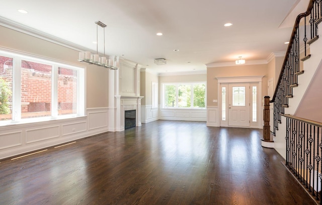 unfurnished living room featuring dark wood finished floors, stairway, a wainscoted wall, a decorative wall, and crown molding