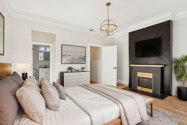 bedroom featuring crown molding, an inviting chandelier, light wood finished floors, a fireplace, and visible vents