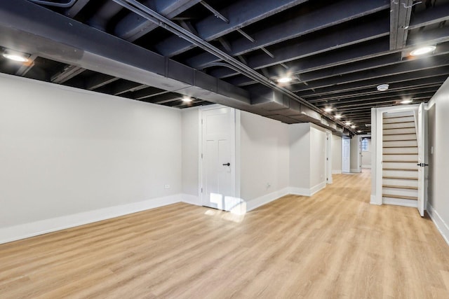 finished basement featuring baseboards, stairs, and light wood-style flooring