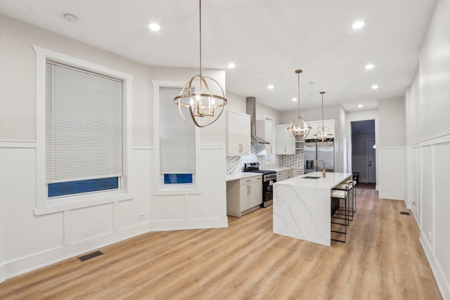kitchen featuring stainless steel appliances, a sink, visible vents, a notable chandelier, and wall chimney range hood