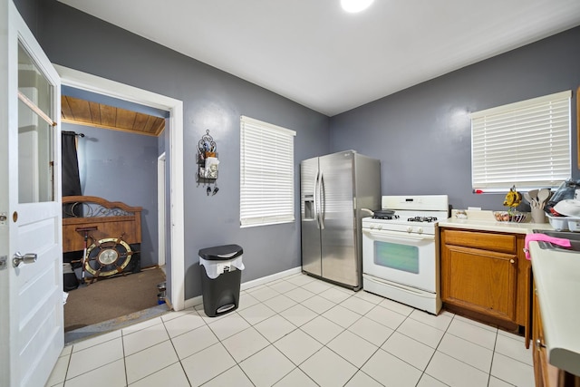 kitchen featuring stainless steel fridge, baseboards, white range with gas cooktop, brown cabinets, and light countertops