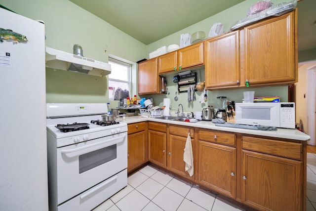 kitchen featuring under cabinet range hood, a sink, white appliances, and light tile patterned floors