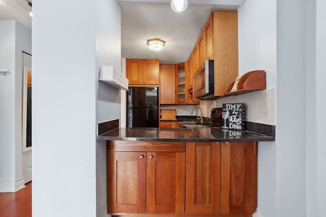 kitchen with brown cabinetry, freestanding refrigerator, stainless steel microwave, a peninsula, and glass insert cabinets