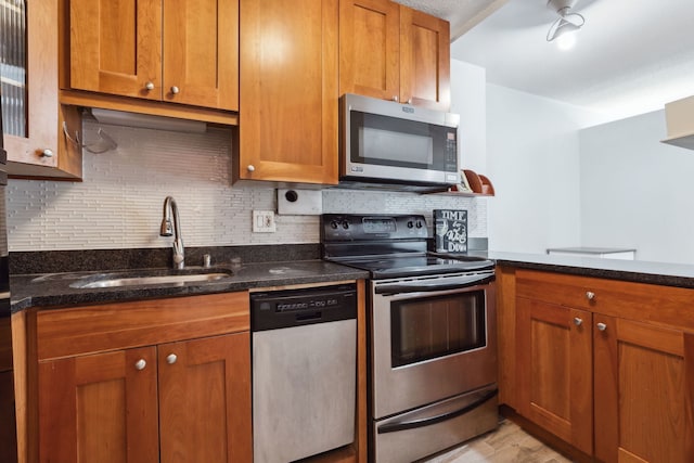 kitchen with appliances with stainless steel finishes, tasteful backsplash, brown cabinets, a sink, and dark stone countertops