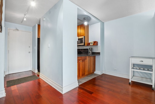 kitchen featuring brown cabinetry, dark wood finished floors, stainless steel microwave, and dark countertops