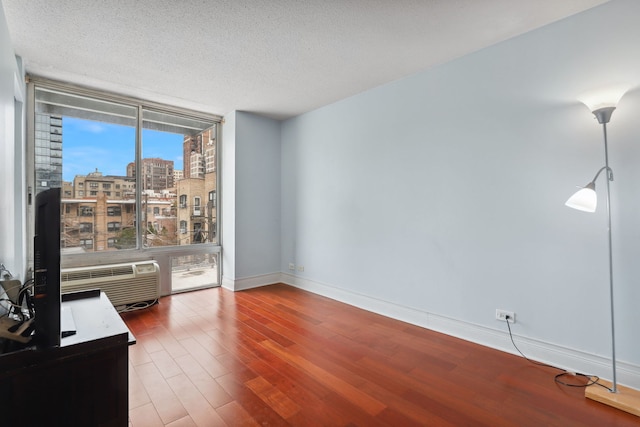 empty room featuring an AC wall unit, a textured ceiling, baseboards, wood finished floors, and expansive windows