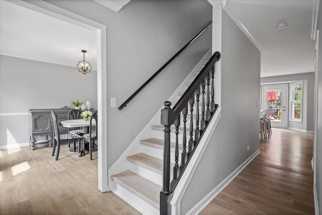 stairway with crown molding, baseboards, wood finished floors, and a chandelier