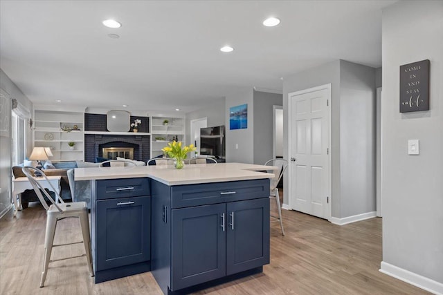 kitchen with a breakfast bar, baseboards, open floor plan, light wood-style floors, and light countertops