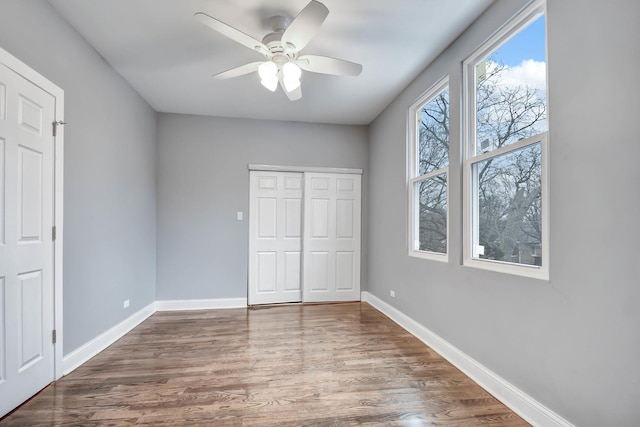unfurnished bedroom featuring wood finished floors, a closet, baseboards, and ceiling fan
