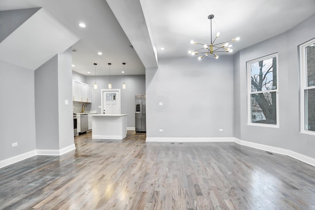 unfurnished living room featuring baseboards, a notable chandelier, wood finished floors, and recessed lighting
