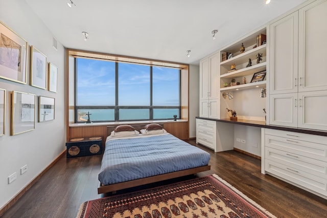 bedroom with a water view, dark wood finished floors, visible vents, baseboards, and built in study area