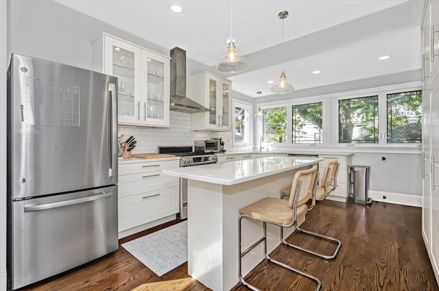 kitchen featuring white cabinetry, appliances with stainless steel finishes, light countertops, wall chimney exhaust hood, and dark wood-type flooring