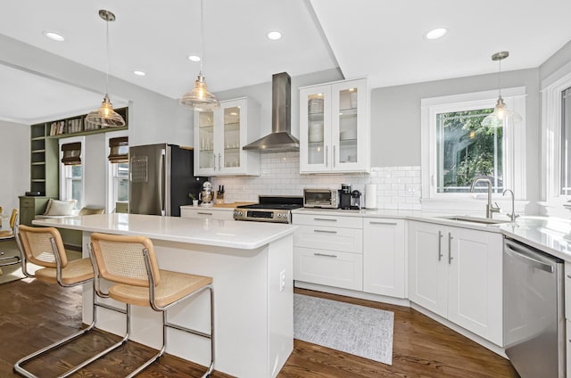 kitchen featuring dark wood-style floors, a sink, glass insert cabinets, wall chimney exhaust hood, and appliances with stainless steel finishes