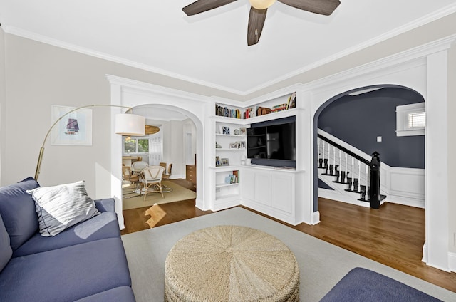 living area featuring stairs, arched walkways, ornamental molding, and wood finished floors