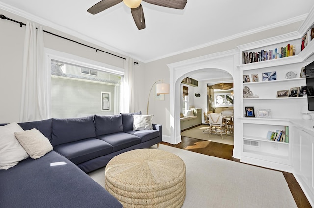 living area with wood finished floors, a healthy amount of sunlight, crown molding, and arched walkways