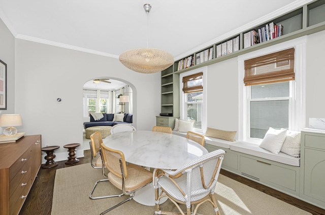 dining area with crown molding, arched walkways, wood finished floors, and a healthy amount of sunlight