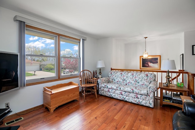 living area with wood-type flooring, visible vents, baseboards, and plenty of natural light
