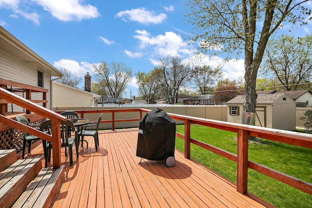 deck featuring fence, an outbuilding, outdoor dining space, a lawn, and a grill