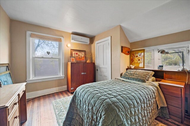 bedroom featuring hardwood / wood-style flooring, baseboards, an AC wall unit, and a closet
