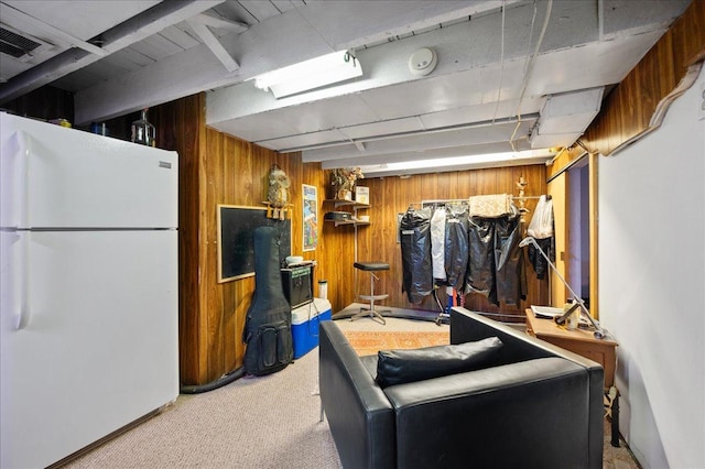 finished below grade area with visible vents, freestanding refrigerator, carpet, and wood walls