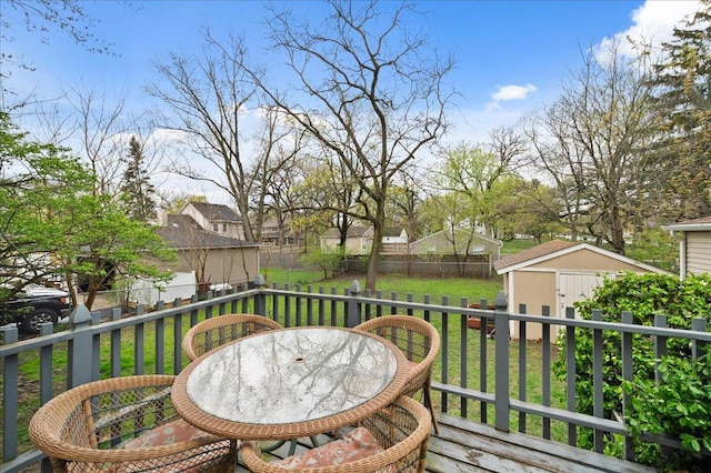 wooden terrace with a shed, a lawn, outdoor dining space, a fenced backyard, and an outbuilding