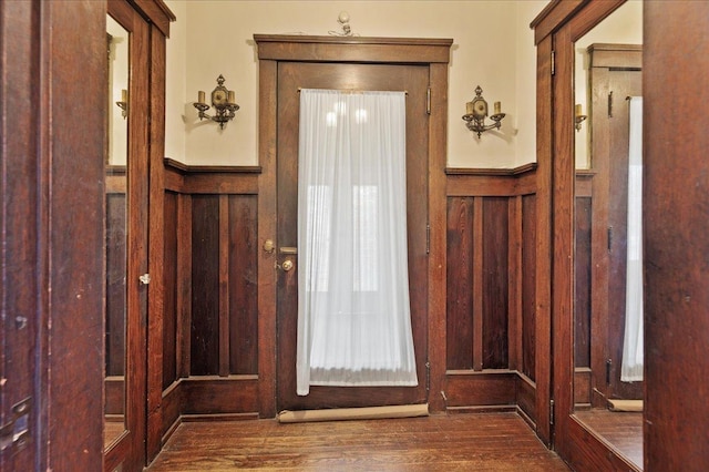doorway with wood finished floors, a decorative wall, and wainscoting