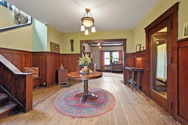 interior space with light wood finished floors, a wainscoted wall, an inviting chandelier, wood walls, and stairway