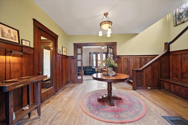 entryway with light wood-style flooring, wood walls, french doors, and wainscoting