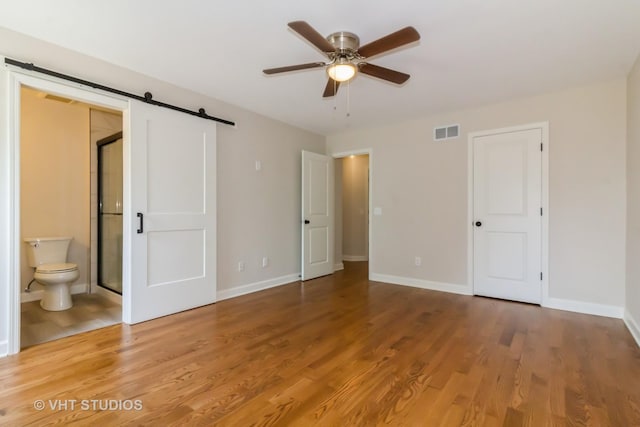2509 Oak Trails Dr, Aurora, IL 60506 - unfurnished bedroom with a barn door, wood finished floors, ensuite bathroom, and a ceiling fan