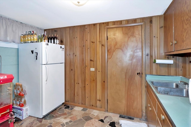 kitchen with freestanding refrigerator, stone finish flooring, brown cabinets, and wooden walls