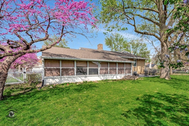 rear view of house featuring fence, a chimney, a sunroom, a shingled roof, and a lawn