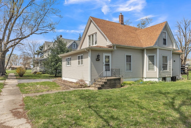 rear view of house featuring a chimney, a shingled roof, and a lawn