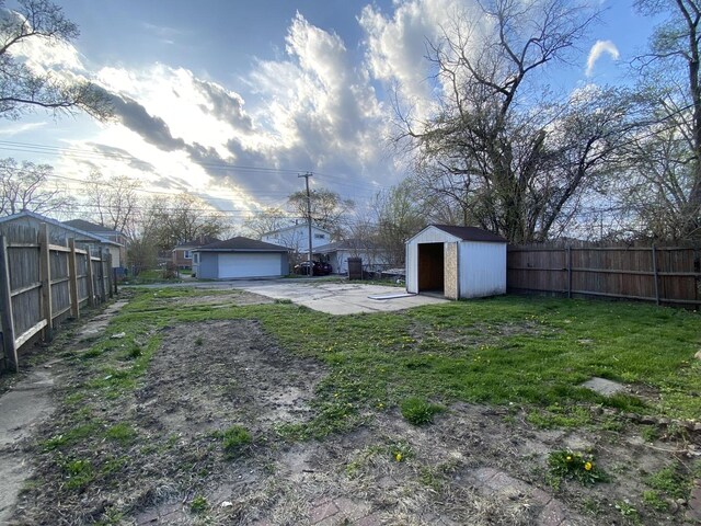 view of yard featuring fence, an outbuilding, a detached garage, and a storage shed