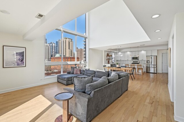 living area with visible vents, baseboards, a city view, light wood finished floors, and recessed lighting
