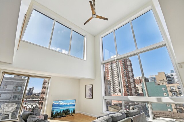 living area featuring a healthy amount of sunlight, ceiling fan, wood finished floors, a view of city, and a high ceiling