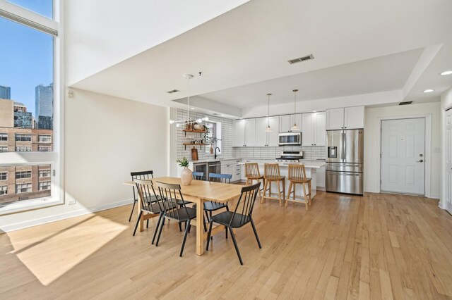 dining area with visible vents, light wood-style flooring, a notable chandelier, and a tray ceiling