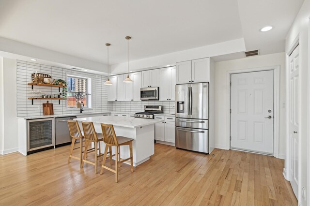 kitchen with a kitchen bar, visible vents, appliances with stainless steel finishes, tasteful backsplash, and wine cooler