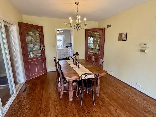 dining space with dark wood finished floors, baseboards, a chandelier, and visible vents