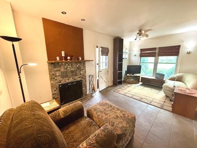 tiled living room with a fireplace and ceiling fan
