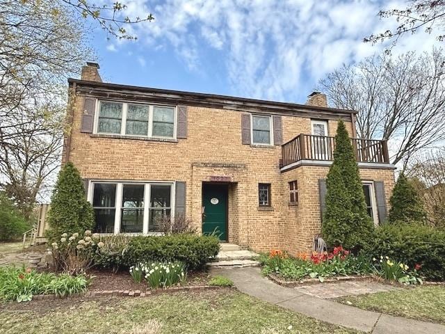 view of front of house with a chimney, brick siding, and a balcony