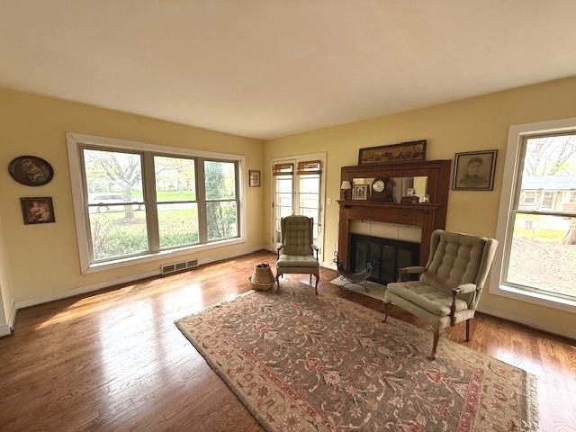 living area with a fireplace with flush hearth, baseboards, wood finished floors, and visible vents